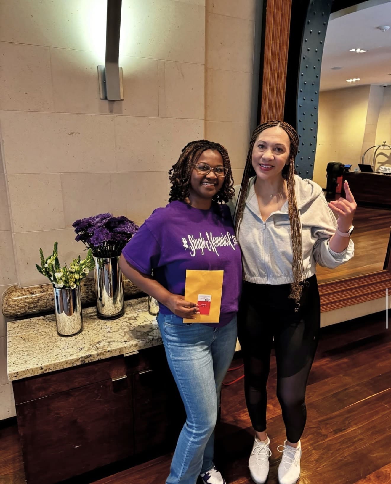 Two women smiling indoors, holding envelopes.