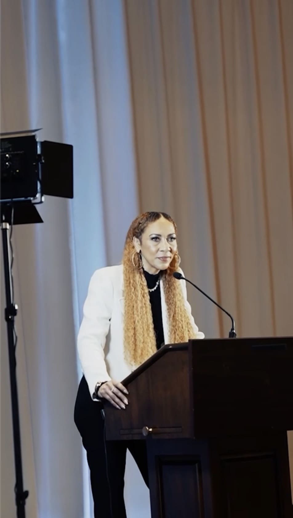 Person speaking at a podium, white jacket.