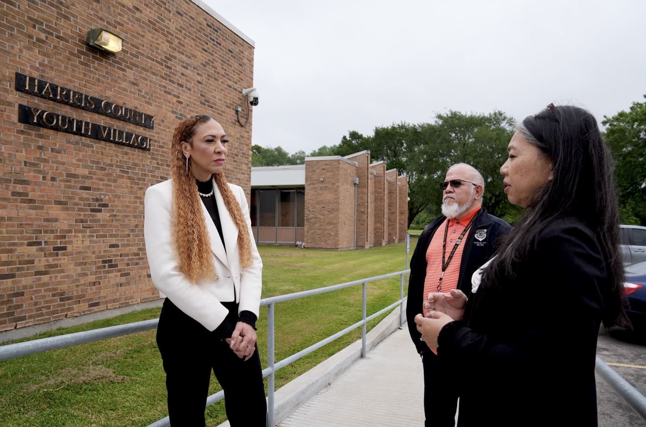 Three people talking outside a youth village.