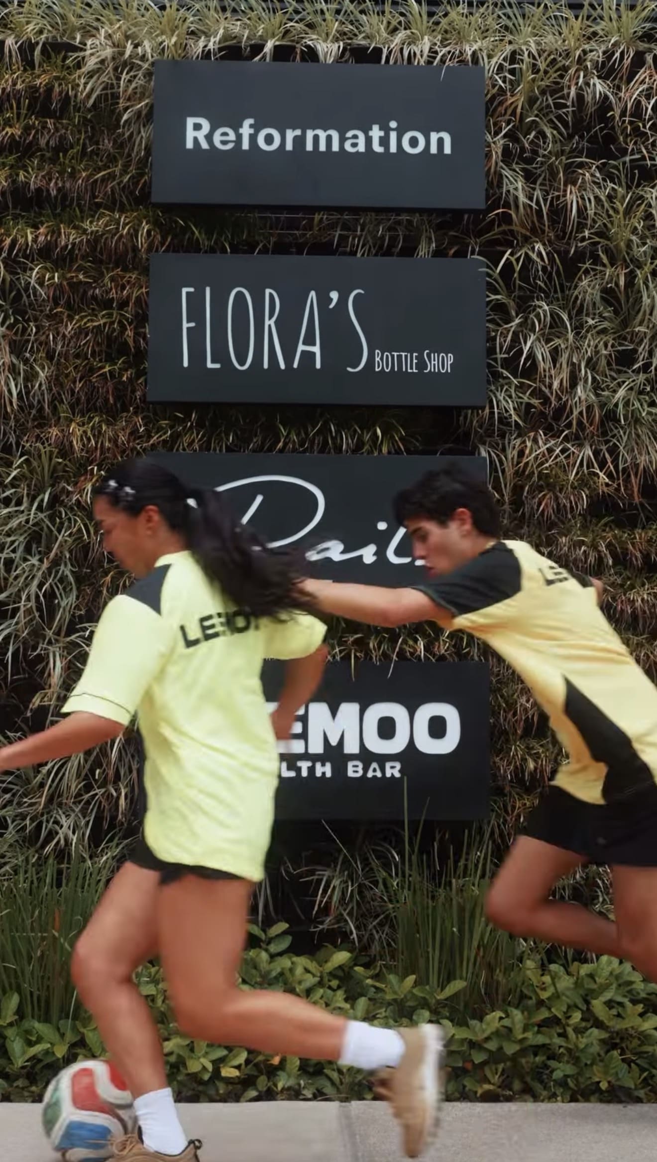 Two people playing soccer near shop signs.
